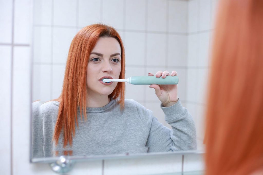 A woman brushes her teeth in the mirror. 